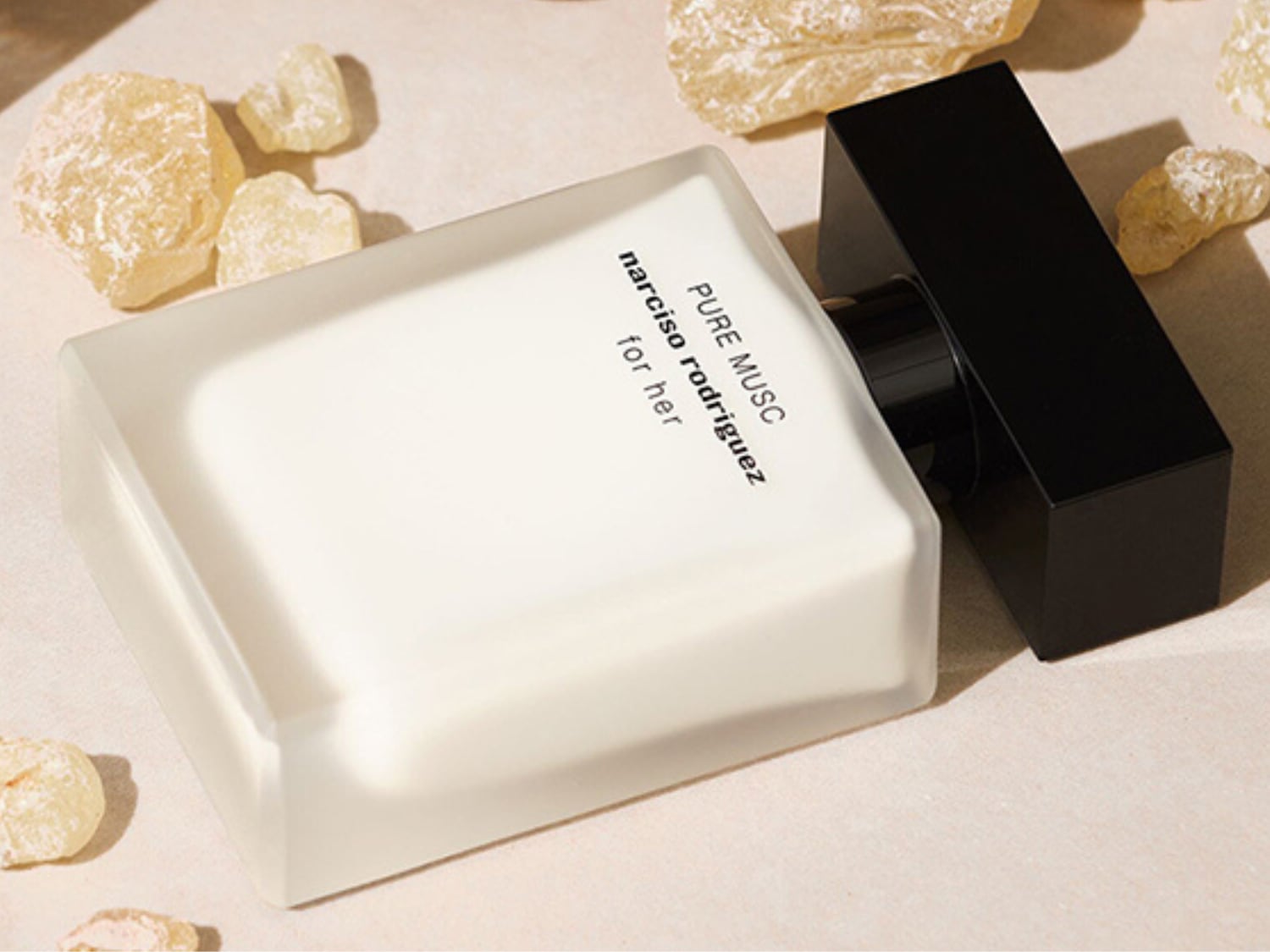 Perfumy Narciso Rodriguez Pure Musc for Her w eleganckiej, matowej butelce z czarną nakrętką, otoczone bursztynowymi kryształkami, emanują wyrafinowanym zapachem piżma.