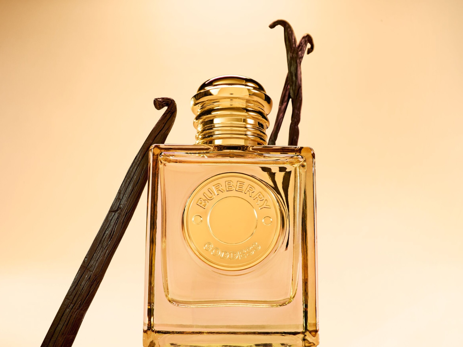 Perfumy Burberry Goddess w eleganckiej, prostokątnej butelce ze złotym korkiem i etykietą, otoczone laskami wanilii, które podkreślają słodki i zmysłowy zapach.