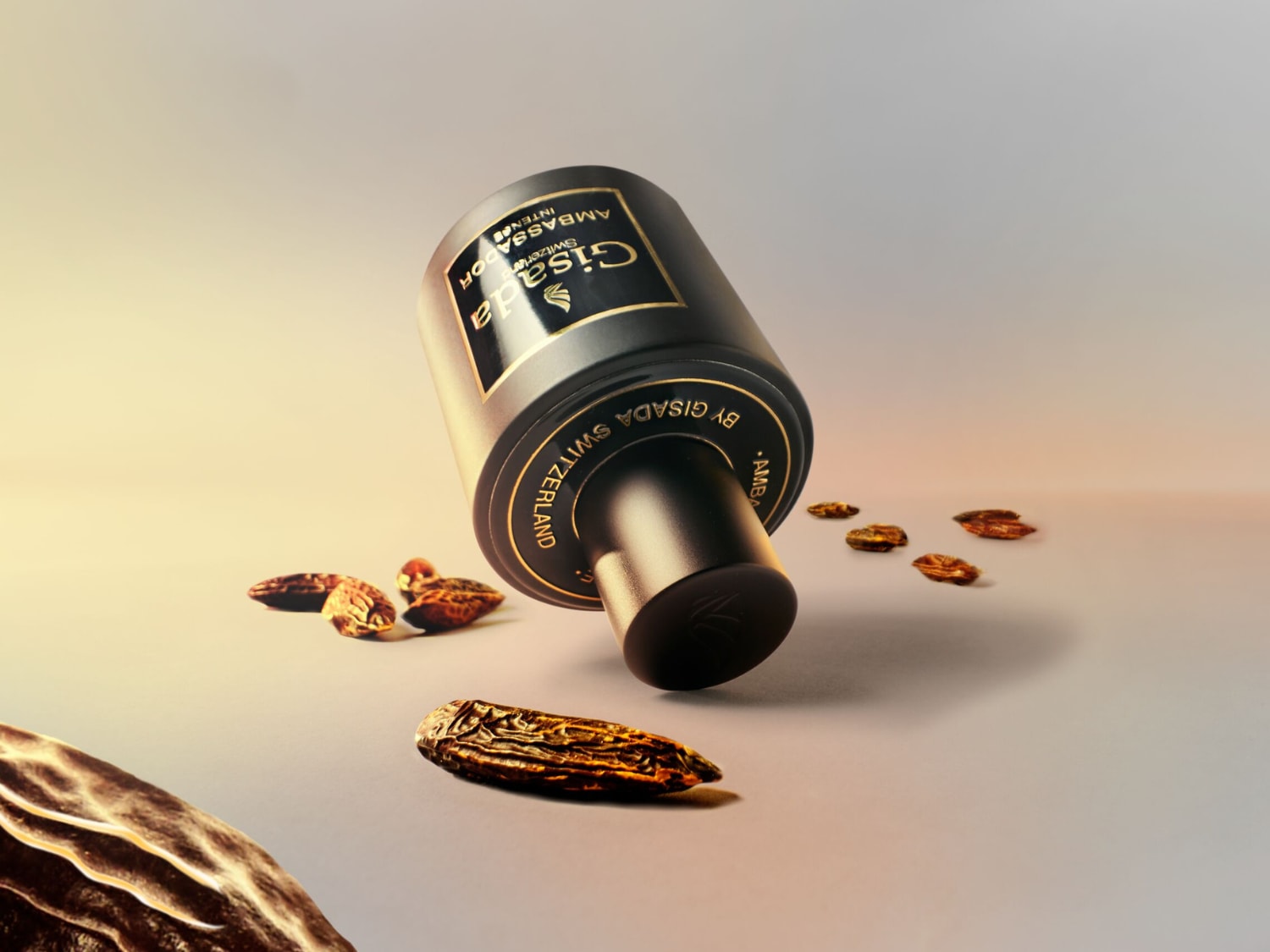Flakon perfum Gisada Ambassador Intense w kolorze czarnym ze złotymi napisami leży na boku, otoczony bursztynowymi kamieniami, na tle z gradientem od jasnego do ciemnego brązu.