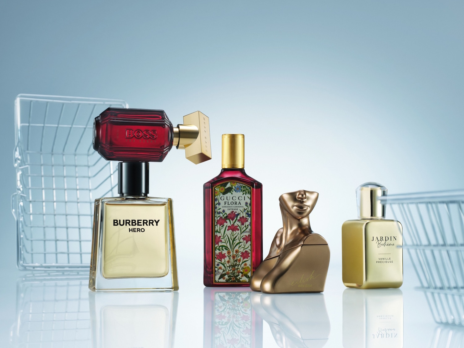 Una collezione di quattro profumi di lusso, tra cui Burberry Hero, Boss The Scent, Gucci Flora Gorgeous Gardenia e Jardin Bohème Vanille Précieuse, sono esposti con cestini della spesa in wireframe sullo sfondo.