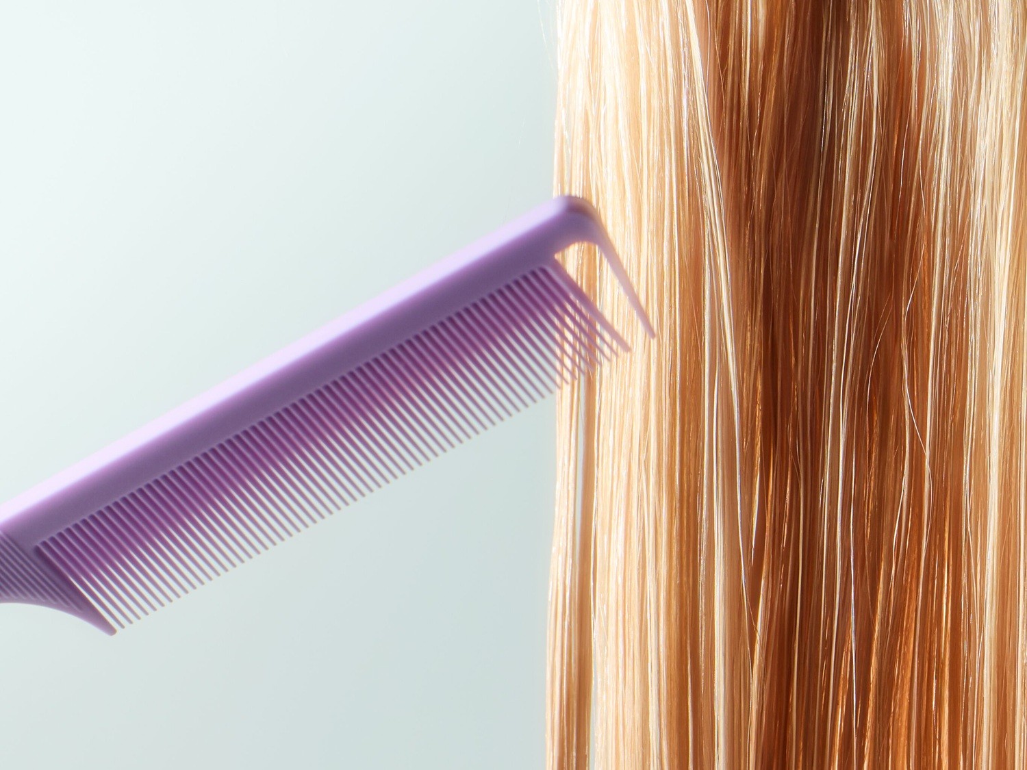 Un pettine viola scorre attraverso una ciocca di capelli biondi lisci e lucidi, mettendo in risalto la morbidezza e la lucentezza della chioma.