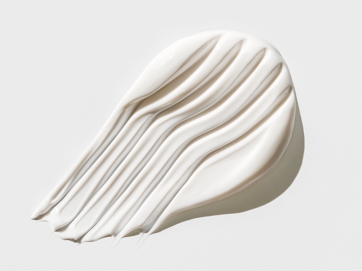 Een dikke, witte crème is in golvende strepen uitgesmeerd op een witte achtergrond, wat de rijke textuur van het product benadrukt.