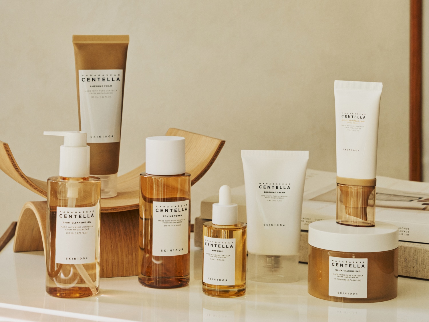 Zestaw produktów do pielęgnacji skóry SKIN1004 Madagascar Centella, w tym pianka do mycia twarzy, olejek oczyszczający, tonik, ampułka, krem łagodzący i płatki uspokajające, wszystkie w neutralnych odcieniach beżu i brązu, stojące na białej powierzchni.