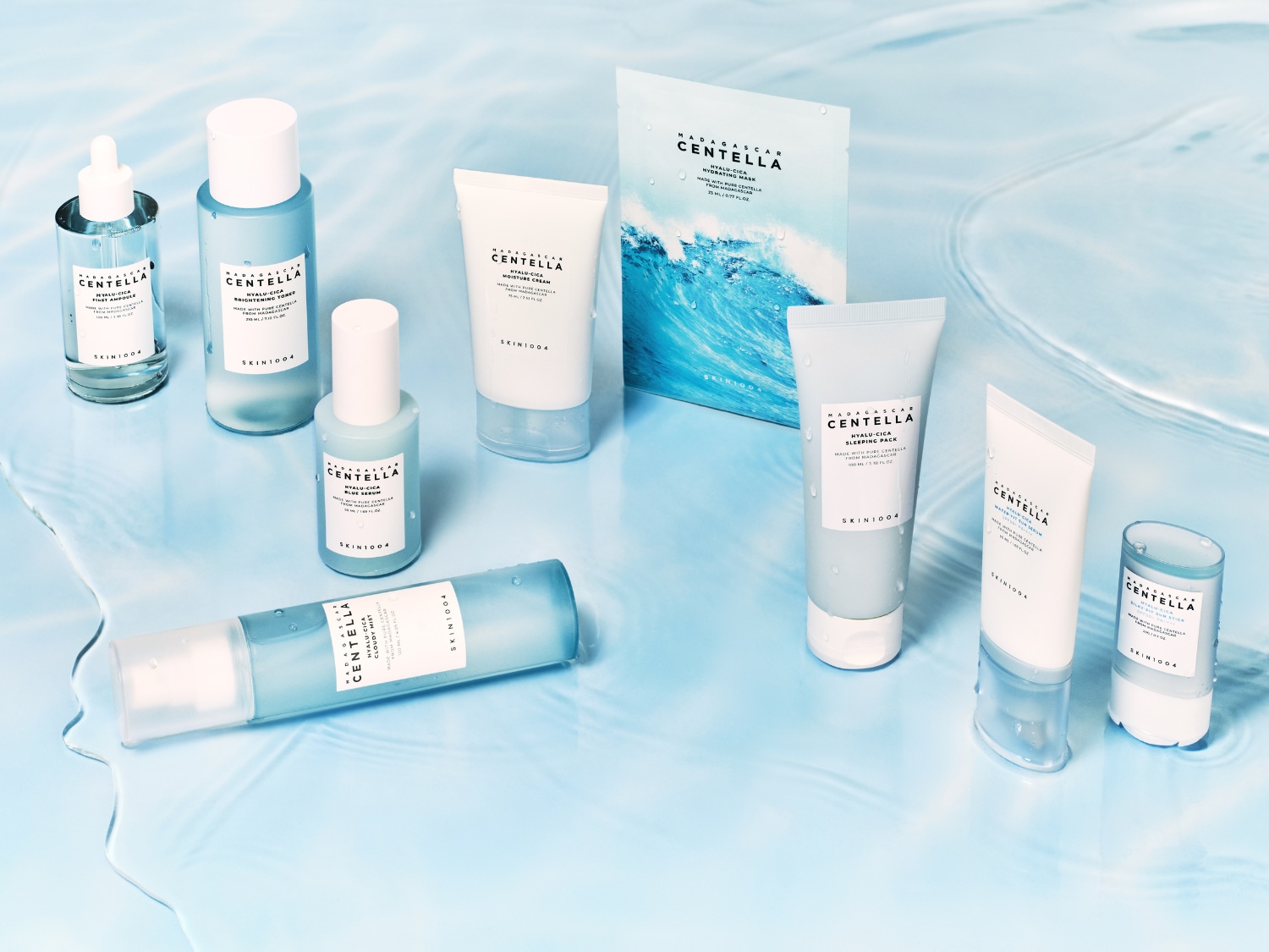 Kolekcja produktów do pielęgnacji skóry Madagascar Centella Hyalu-Cica, w tym serum, tonik, krem nawilżający, maska w płachcie, krem na noc, krem przeciwsłoneczny i sztyft przeciwsłoneczny, wszystkie w odcieniach błękitu i bieli, ułożone na jasnoniebieskiej, falującej powierzchni.