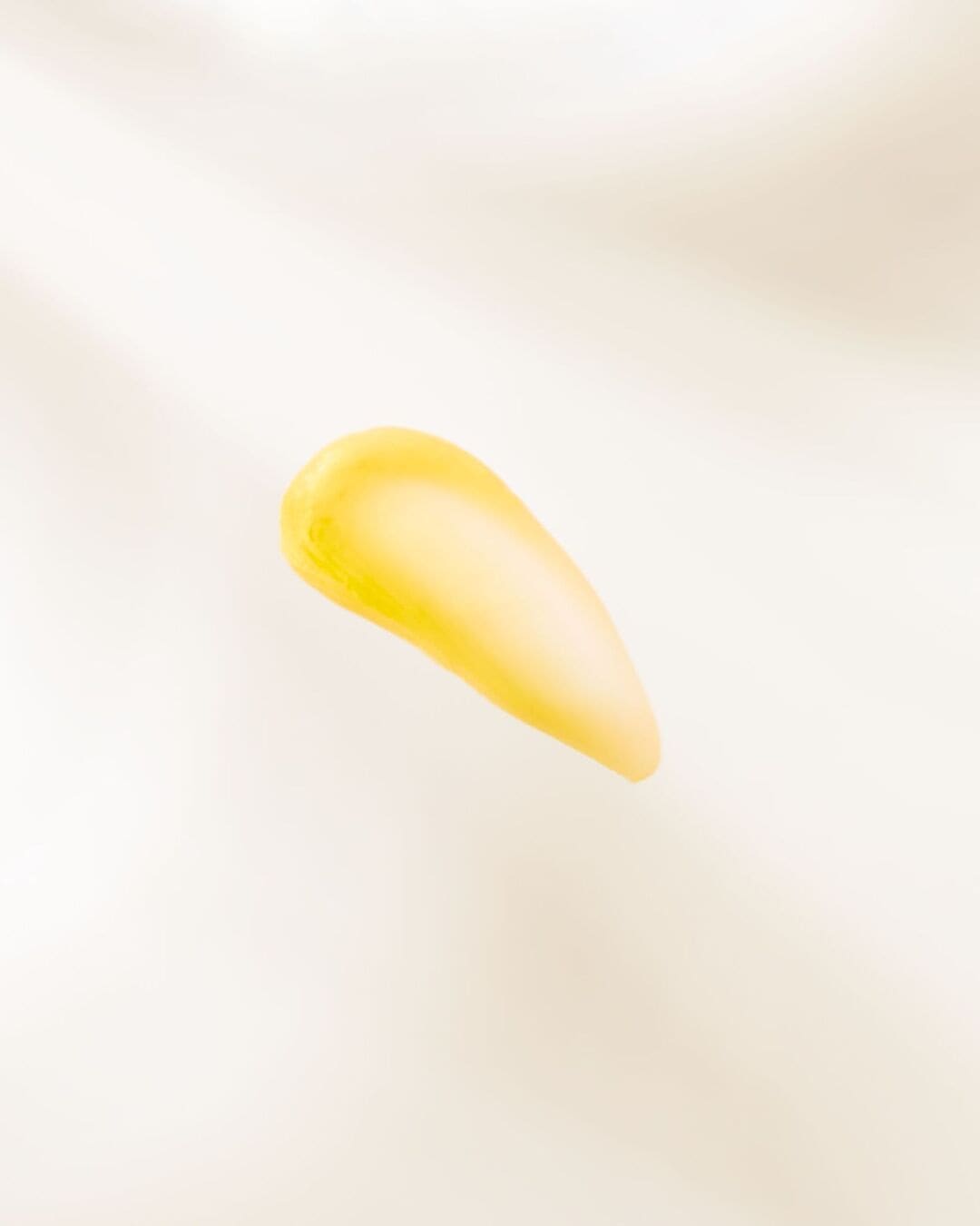 Une goutte de sérum jaune vif est délicatement posée sur une surface blanche, illustrant sa texture riche et sa couleur éclatante.