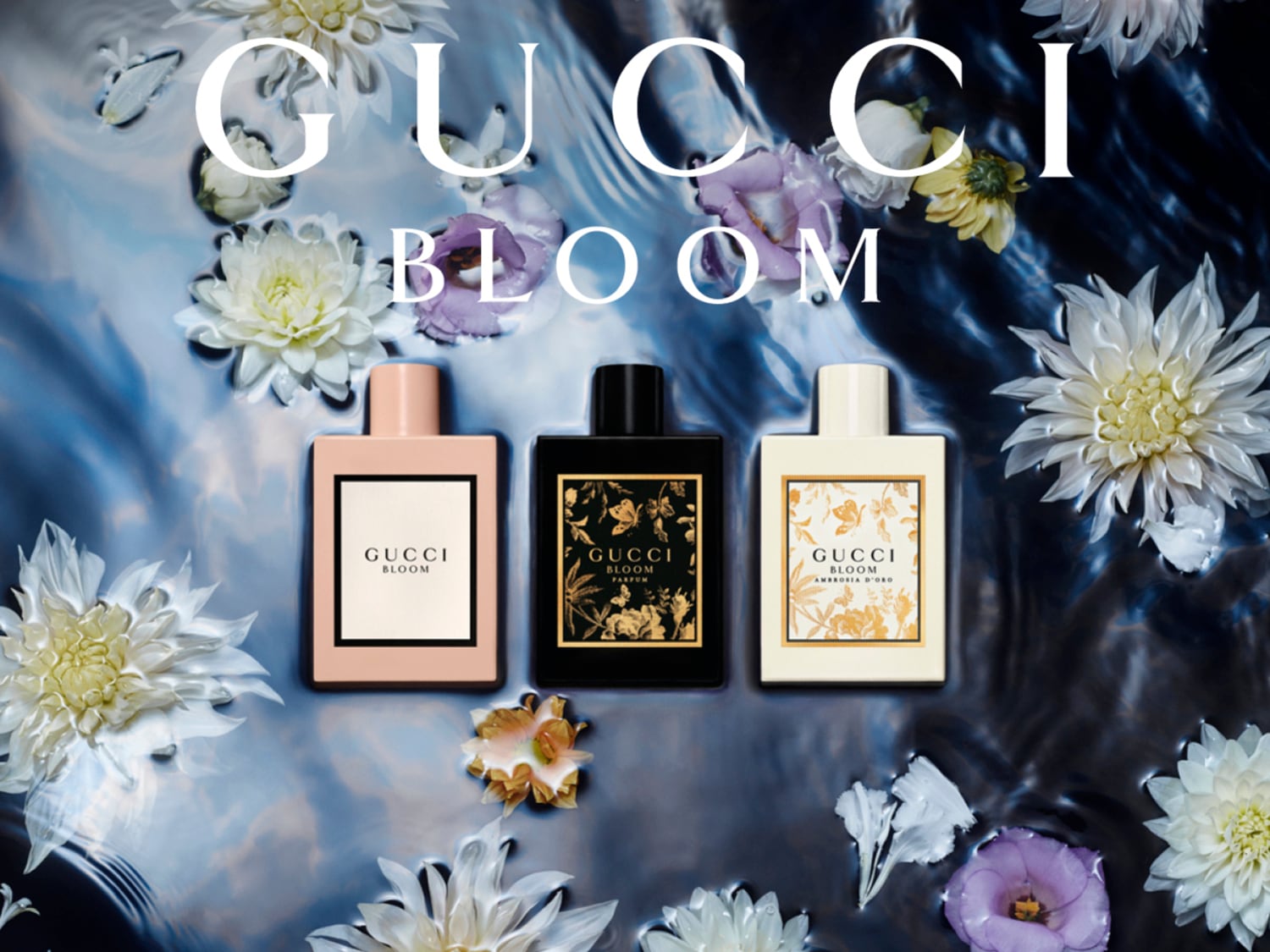Descubre la colección Gucci Bloom, con tres fragancias en envases de color rosa claro, negro y crema, flotando en agua con pétalos de flores blancas y moradas, y el texto "GUCCI BLOOM" en la parte superior.
