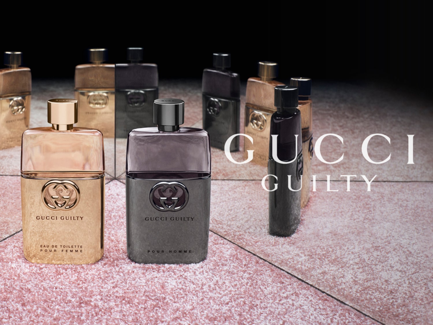 Una colección de fragancias Gucci Guilty, con botellas doradas y grises, se exhibe sobre una superficie brillante, con el logotipo de Gucci Guilty en blanco.