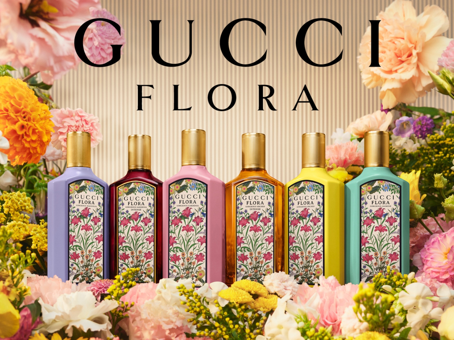 Seis botellas de perfume Gucci Flora de diferentes colores, cada una con una etiqueta floral, se exhiben entre un vibrante arreglo de flores de colores.