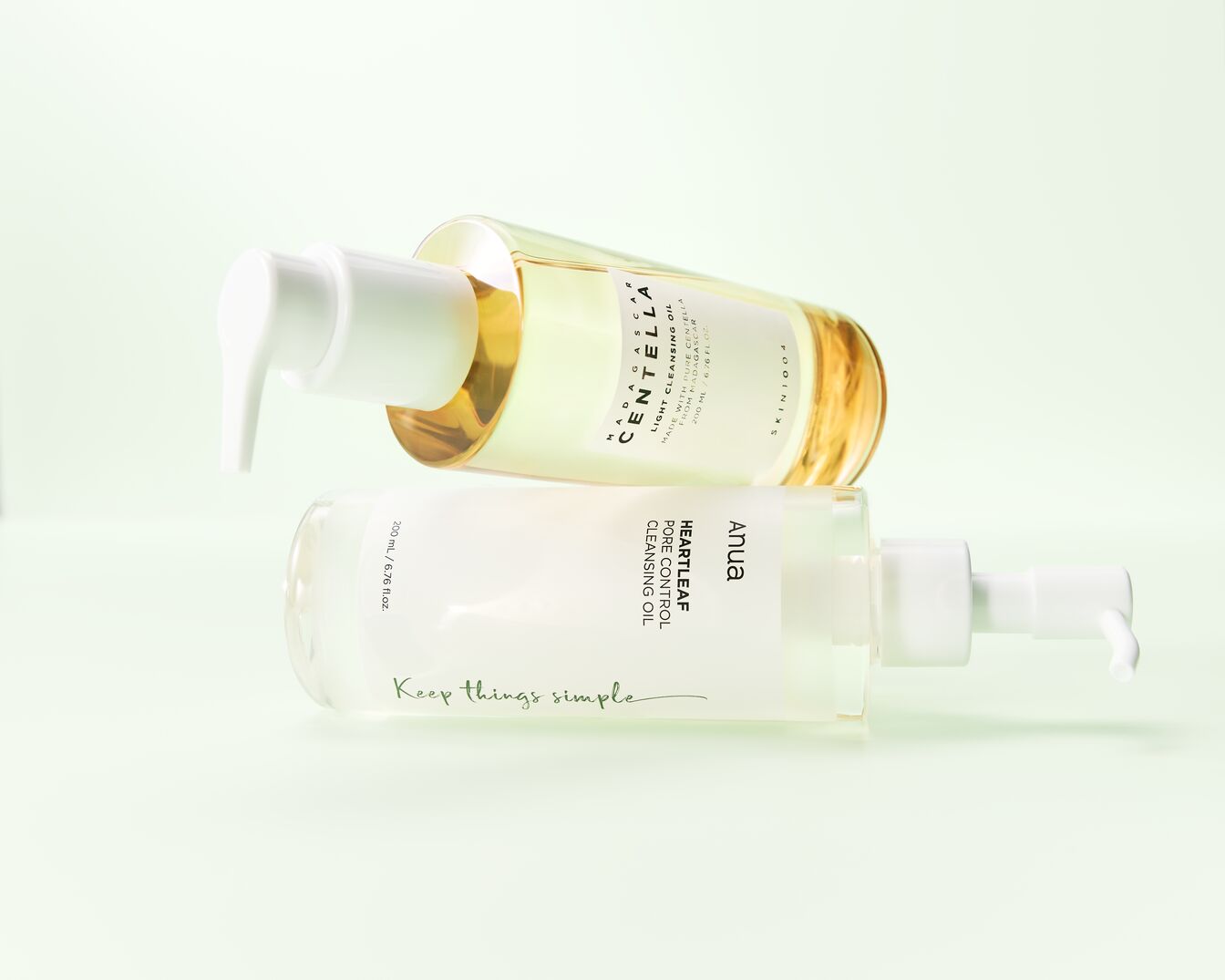 Deux flacons de nettoyant à pompe sont présentés, l'un contenant l'huile nettoyante légère Centella de Madagascar et l'autre l'huile nettoyante Anua Heartleaf Pore Control, tous deux de 200 ml, avec la phrase "Keep things simple" écrite en bas.