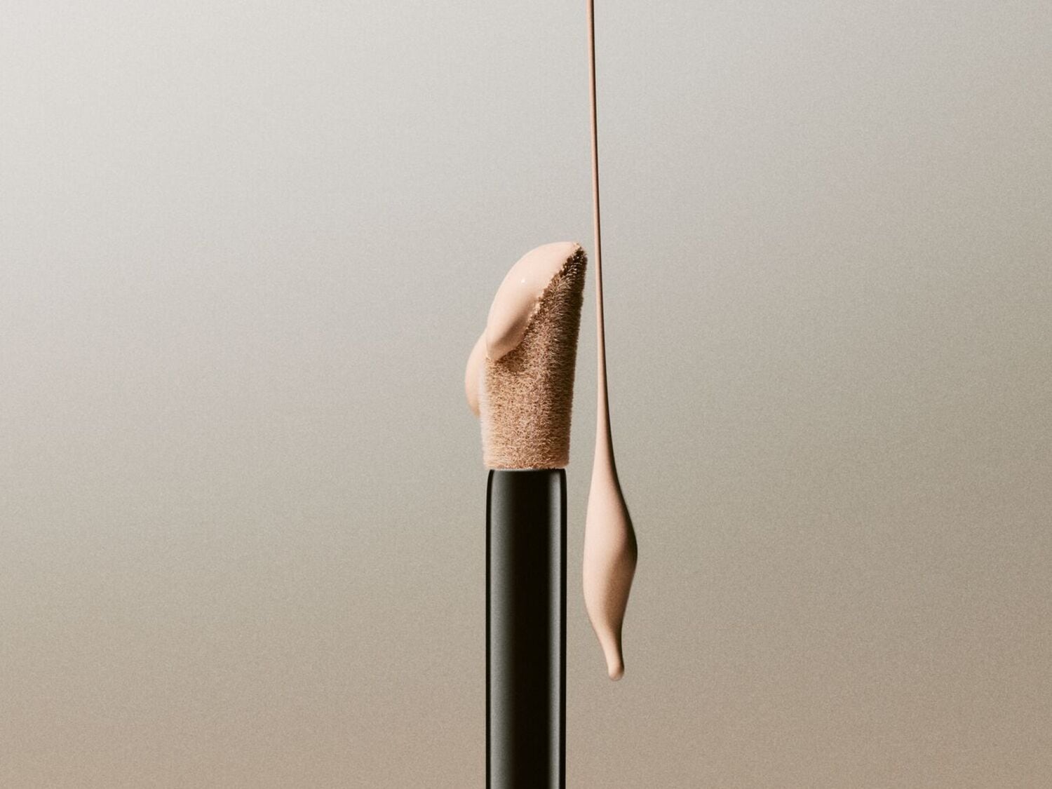 Un applicateur de correcteur avec une texture crémeuse de couleur beige clair, qui coule doucement sur le côté, sur un fond gris clair.
