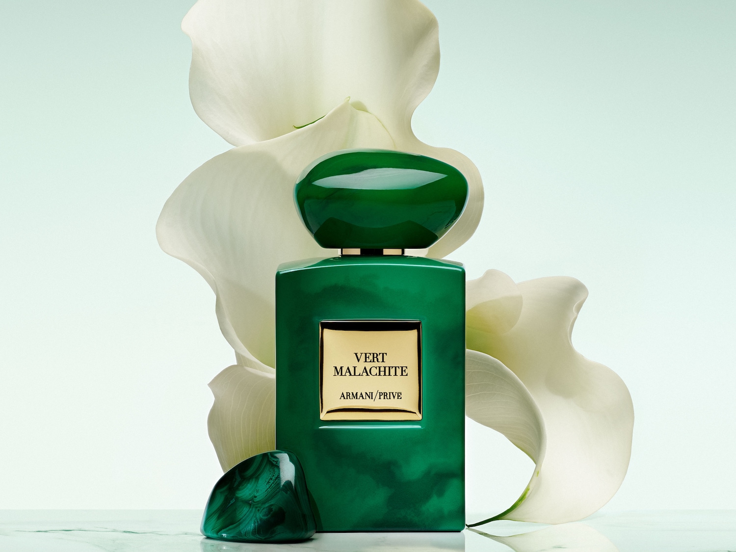 Der Giorgio Armani Vert Malachite Duft präsentiert sich in einem eleganten, rechteckigen, smaragdgrünen Flakon mit einem goldenen Etikett und einem passenden grünen Verschluss, umgeben von weißen Calla-Lilien.