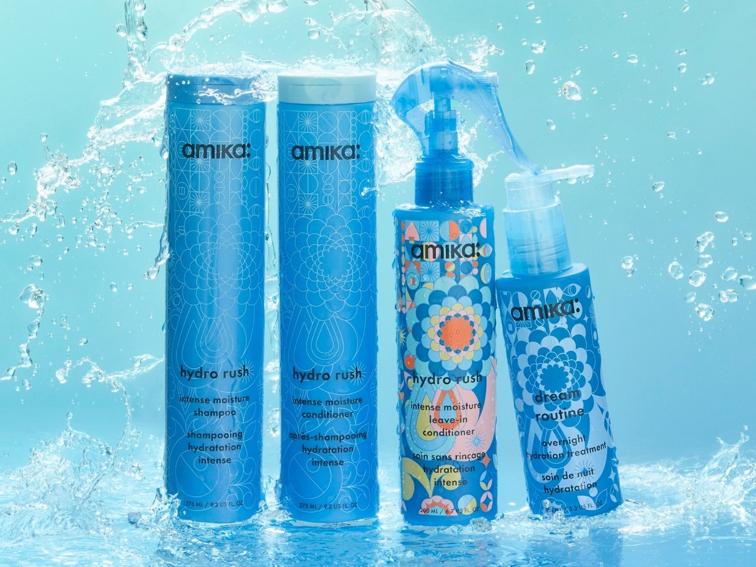 Das Bild zeigt vier blaue Amika Hydro Rush Produkte, darunter Shampoo, Conditioner, Leave-in Conditioner und eine Overnight Hydration Treatment, die von Wasserspritzern umgeben sind.