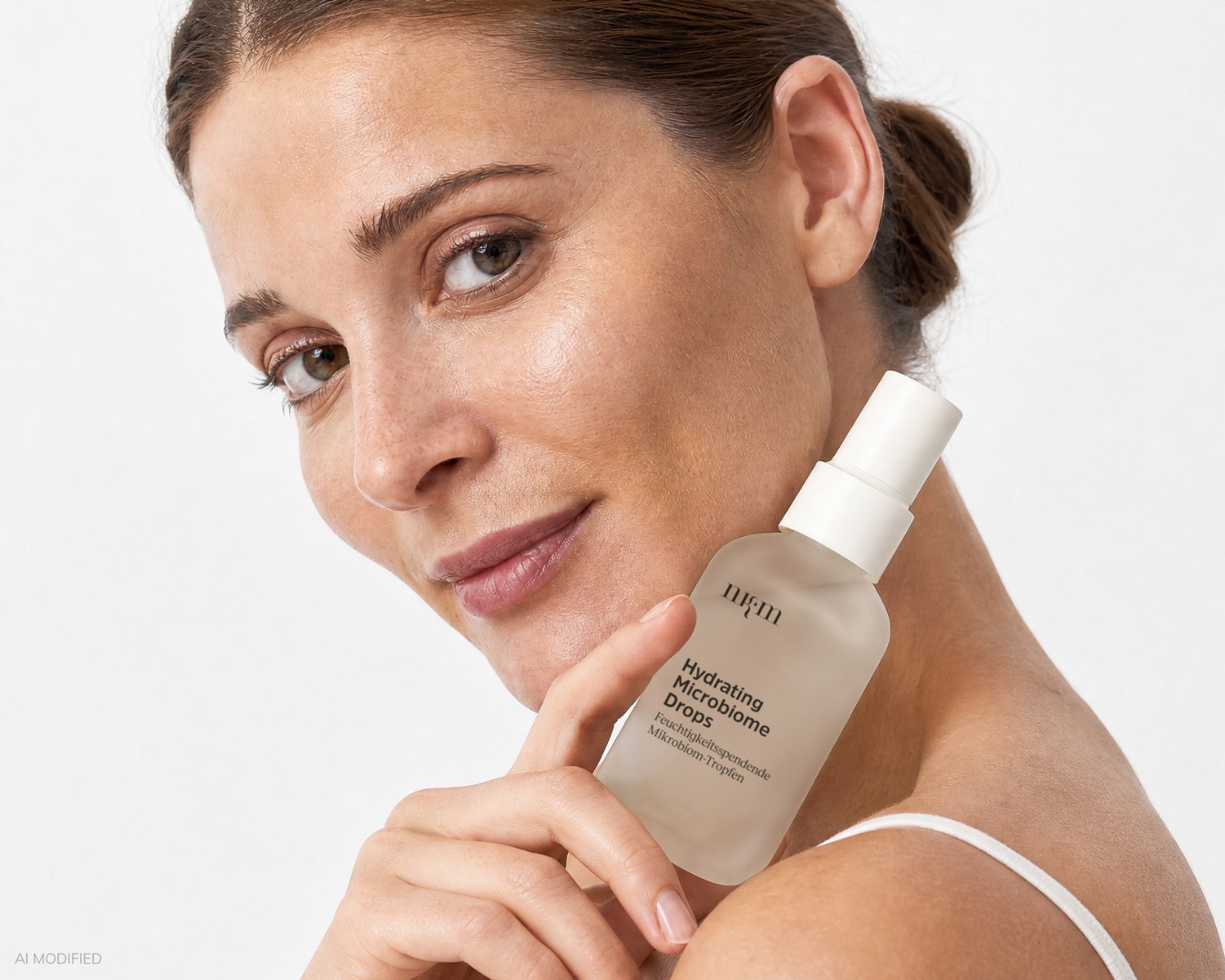 Eine Frau mit glänzender Haut hält eine Flasche nkm Hydrating Microbiome Drops, die Feuchtigkeit spenden und das Mikrobiom der Haut unterstützen.
