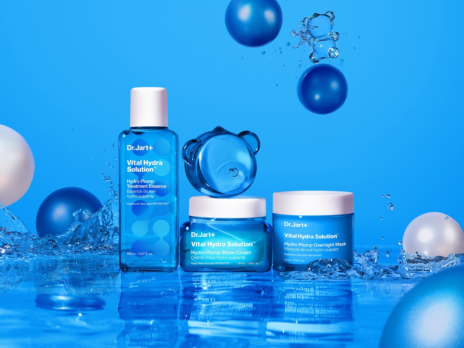 La imagen muestra tres productos Dr.Jart+ Vital Hydra Solution: una esencia de tratamiento, una crema de agua y una mascarilla de noche, todos en envases azules y blancos, rodeados de salpicaduras de agua y esferas azules y blancas.