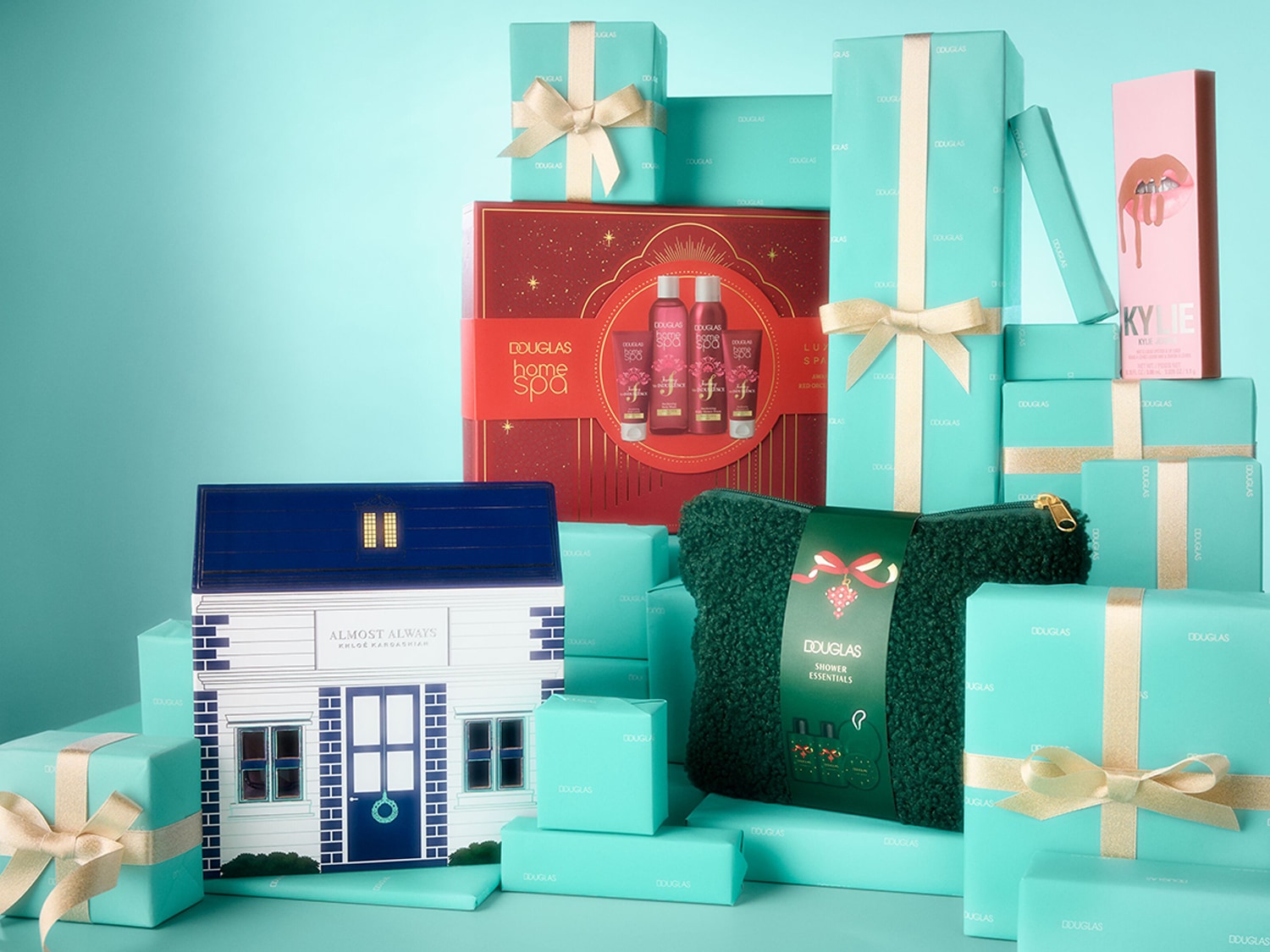 Eine festliche Ansammlung von Douglas-Geschenken in Türkis und Rot, darunter ein "Home Spa"-Set, ein "Shower Essentials"-Beutel und eine Kylie-Kosmetikbox, alle bereit zum Verschenken.