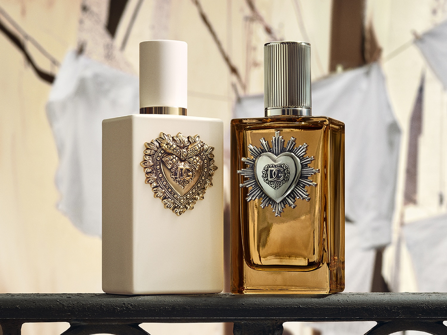 Deux flacons de parfum Dolce & Gabbana, l'un blanc mat avec un cœur doré orné du logo DG, l'autre en verre ambré avec un cœur argenté et le logo DG, posés sur une surface sombre.