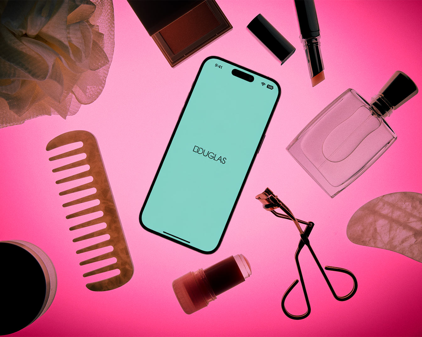 A flat lay of beauty essentials on a vibrant pink background, featuring a smartphone displaying the Douglas logo, a wooden comb, a loofah, a blush compact, a lipstick, a perfume bottle, an eyelash curler, a solid perfume stick, and a gua sha tool.