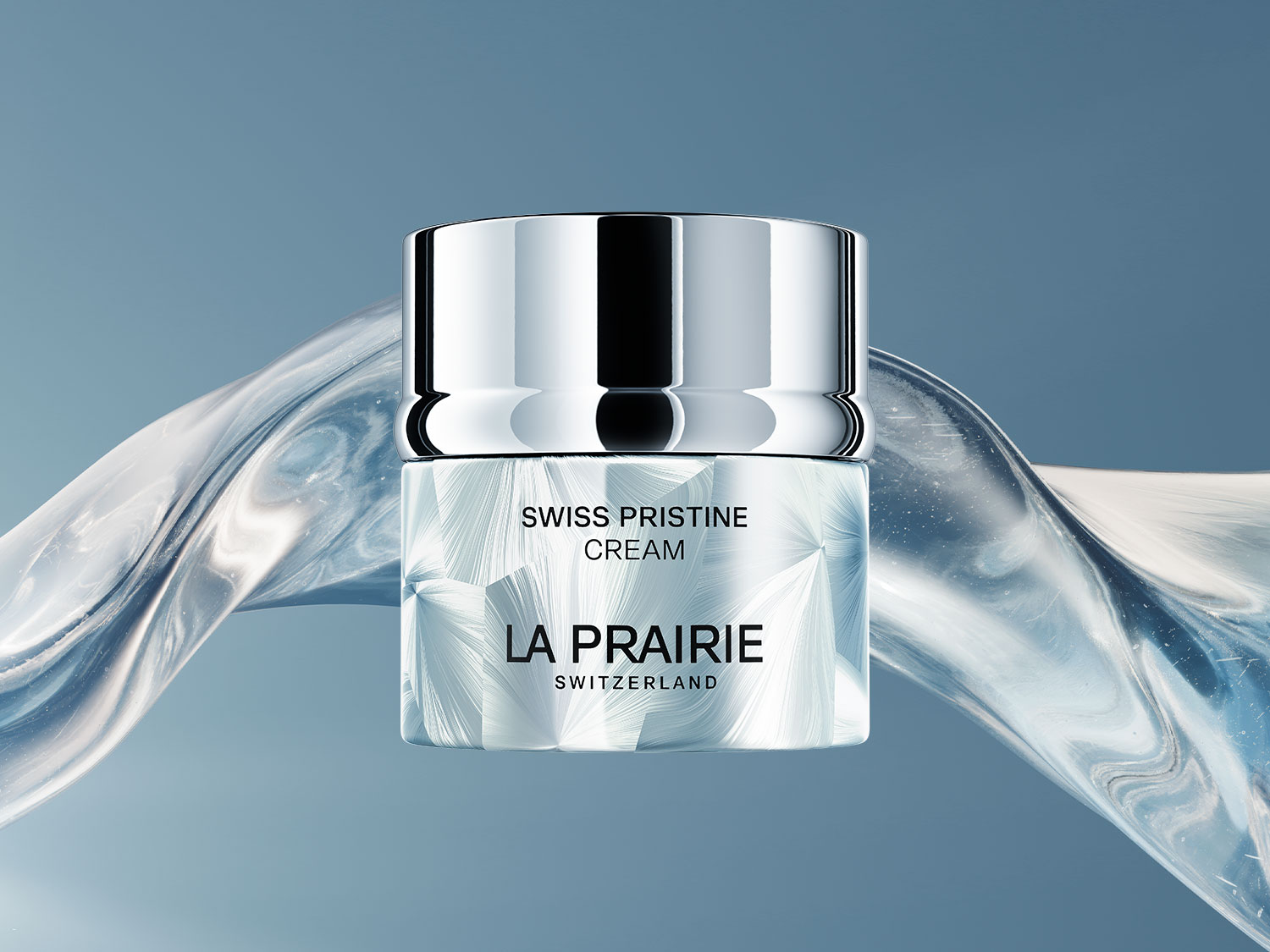 Die La Prairie Swiss Pristine Cream in einem eleganten, silbernen Tiegel mit einem glänzenden Deckel und einem eisblauen, kristallinen Muster auf dem Glas, umgeben von einer fließenden, durchscheinenden blauen Welle.