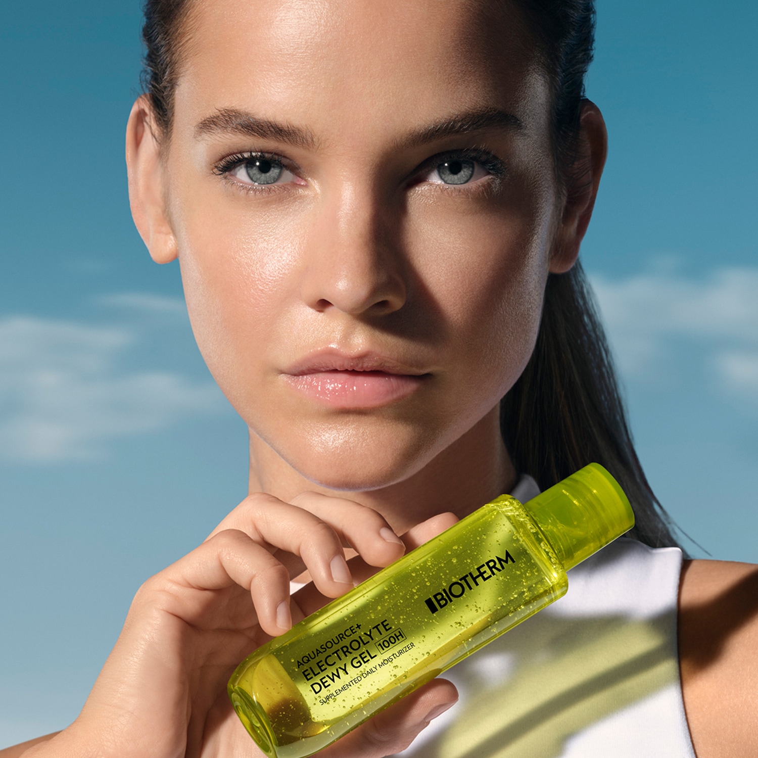 Žena s lesklou pleťou drží v ruke žiarivo žltý hydratačný gél Biotherm Aquasource Electrolyte Dewy Gel 100H, ktorý dodáva pleti hydratáciu a žiarivý vzhľad.