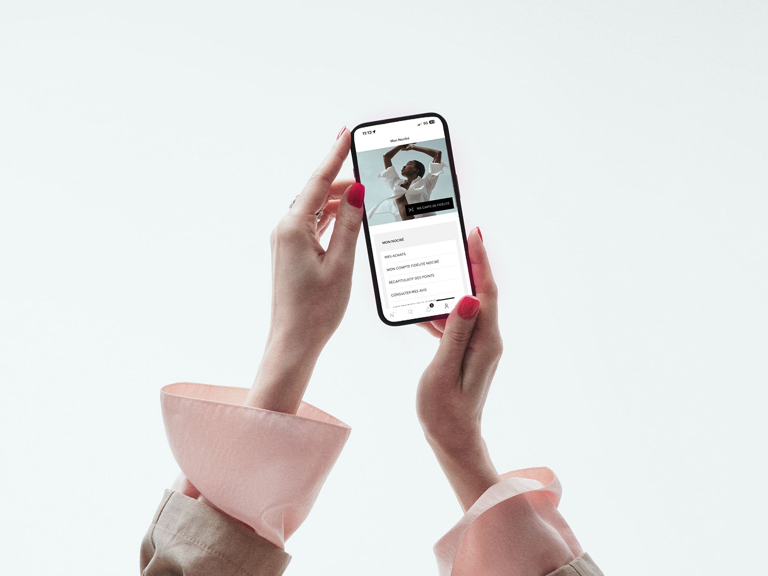 Une personne tient un smartphone affichant l'application Nocibé, avec un menu déroulant présentant les options « Mon Nocibé », « Mes achats », « Mon compte fidélité Nocibé », « Récapitulatif des points » et « Consulter mes avis ».