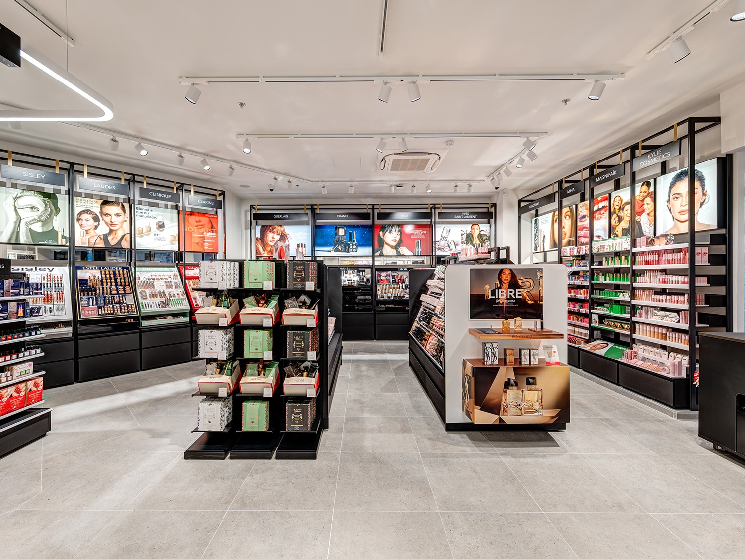 Découvrez un magasin de beauté moderne avec des présentoirs élégants et des étagères remplies de produits de maquillage et de soins de la peau de marques de luxe comme Sisley, Estée Lauder, Clinique et Clarins, le tout sous un éclairage lumineux.