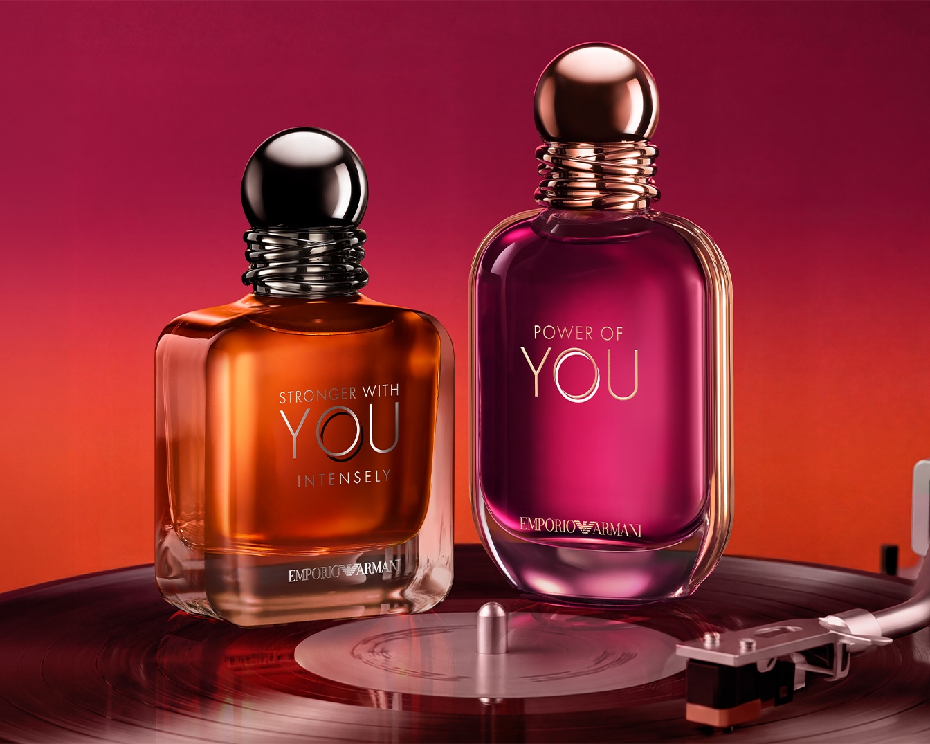 Twee parfumflesjes, één oranje met de tekst "Stronger With You Intensely" en één paars met "Power of You", staan op een platenspeler.
