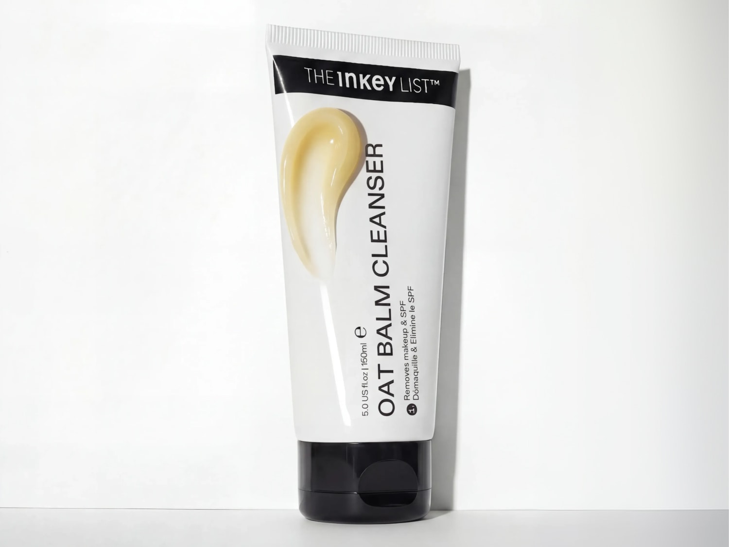 Eine weiße Tube des The Inkey List Oat Balm Cleansers mit schwarzer Schrift steht auf weißem Untergrund und ist mit einem Klecks des cremefarbenen Produkts versehen.