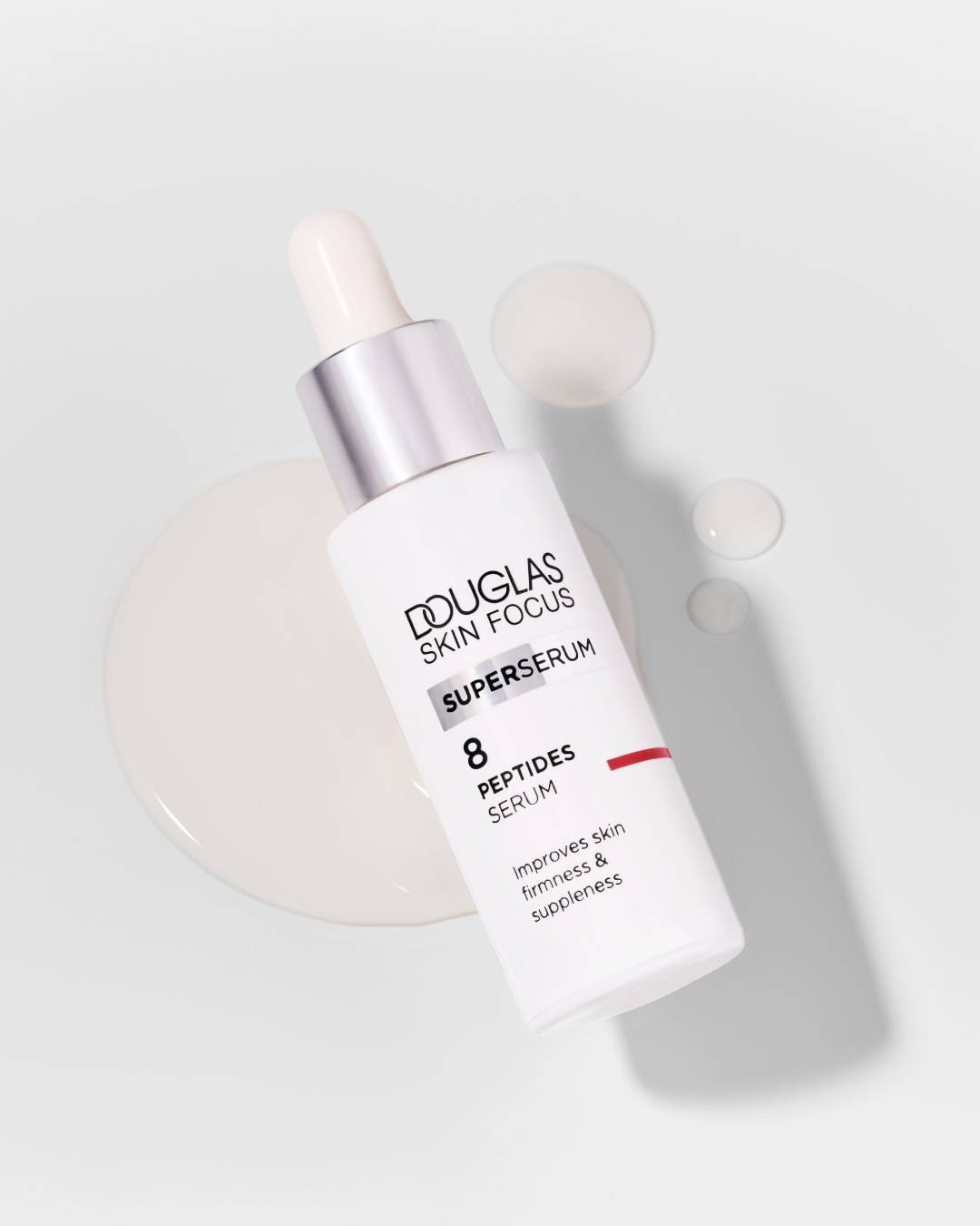 Douglas Skin Focus Superserum 8 Peptides Serum w białej butelce z pipetą, otoczone kroplami serum, poprawia jędrność i elastyczność skóry.