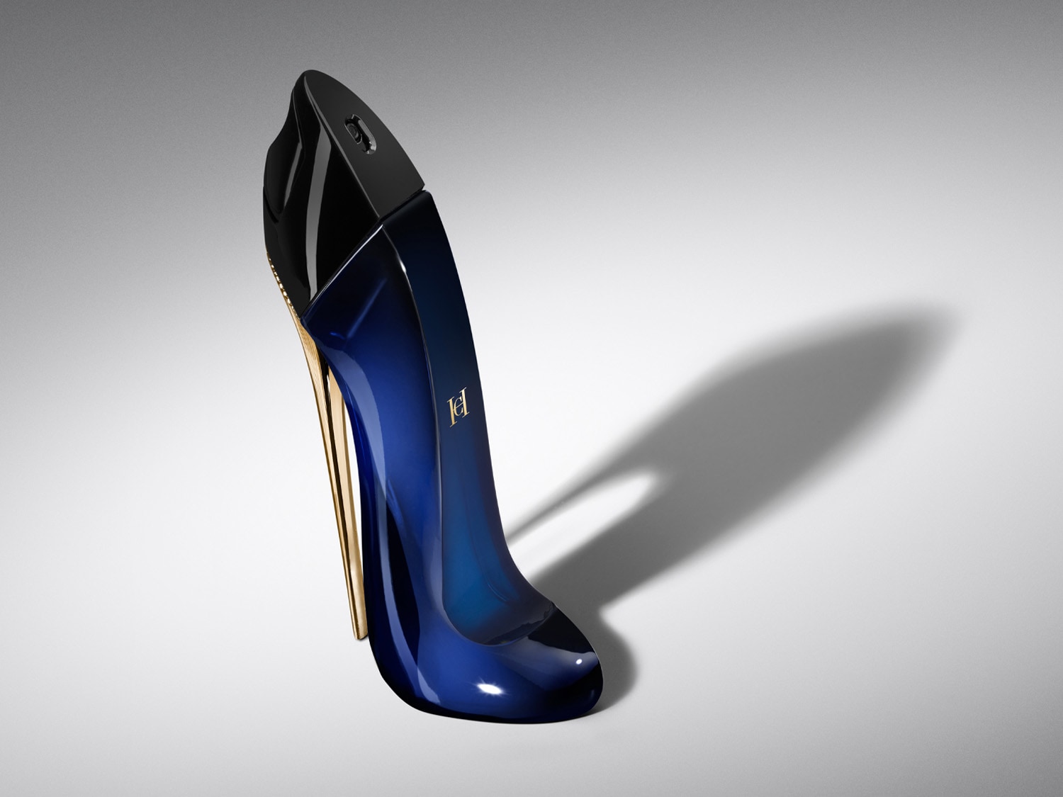 Parfum Carolina Herrera Good Girl v tvare tmavomodrej lodičky s vysokým zlatým podpätkom a čiernou špičkou, s logom značky na boku, je zobrazený na bielom pozadí s tieňom.