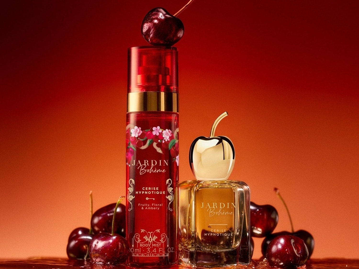 Dwa produkty Jardin Bohème Cerise Hypnotique, mgiełka do ciała i perfumy, stoją na tle w kolorze czerwono-pomarańczowym, otoczone wiśniami, z jedną wiśnią na szczycie mgiełki.