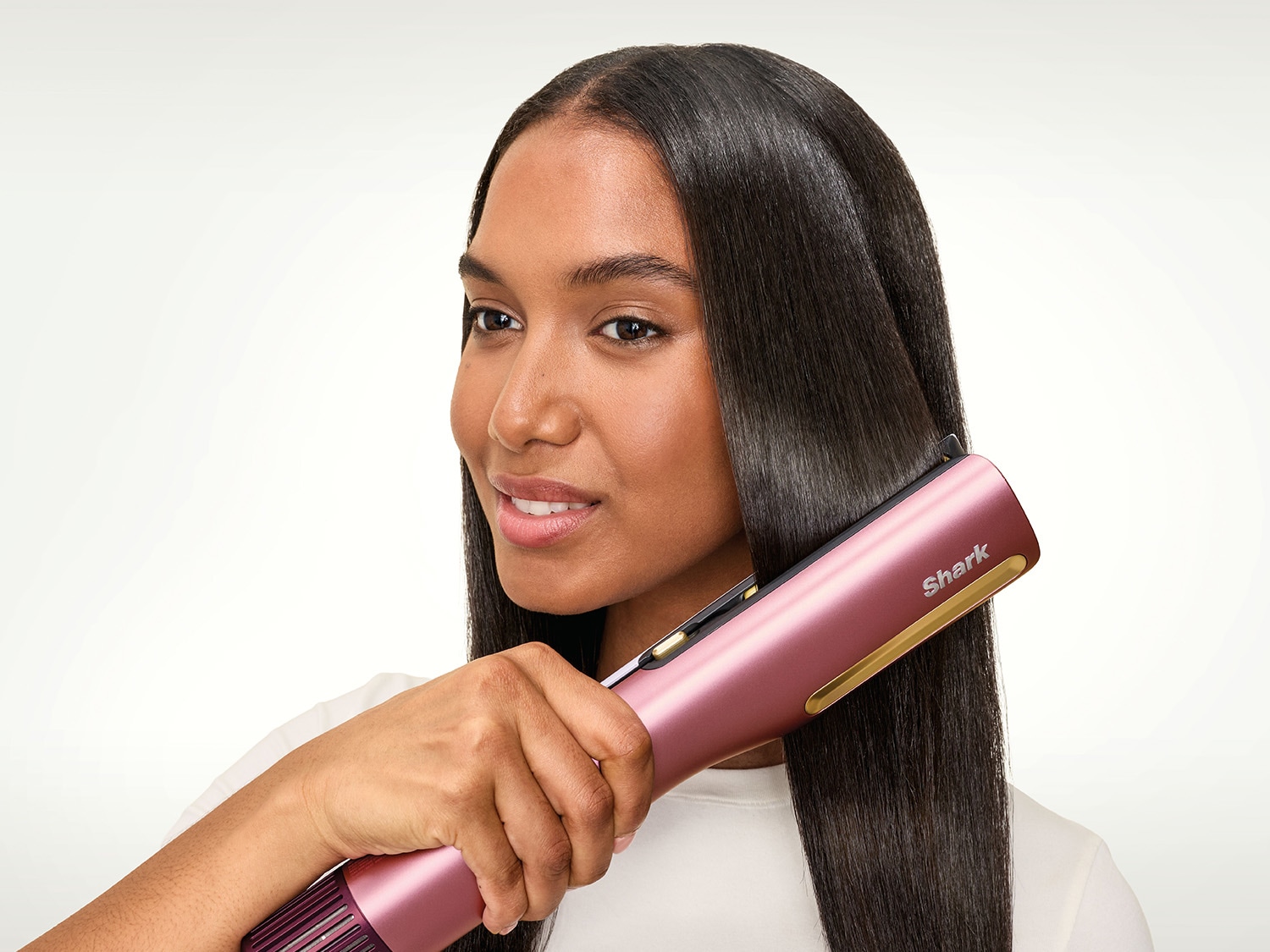 Une femme aux cheveux lisses et brillants utilise un lisseur Shark rose et doré, mettant en valeur la facilité d'utilisation et les résultats professionnels de l'appareil.