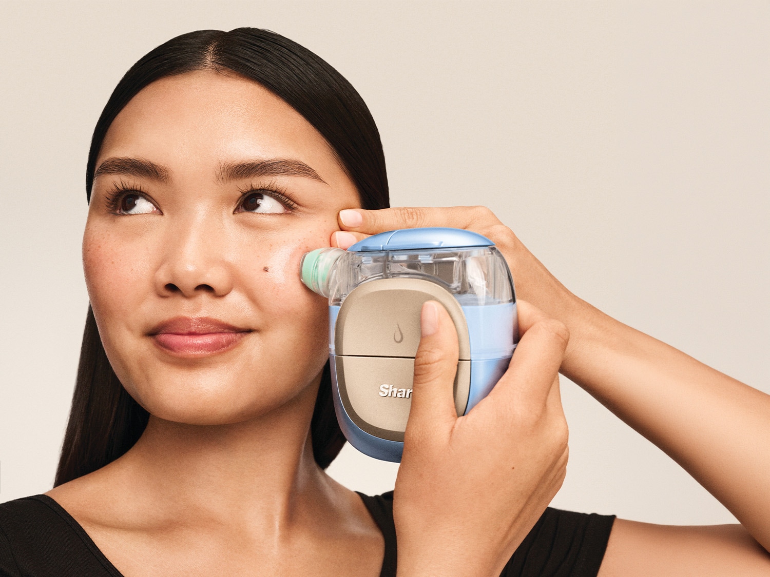 Une femme utilise un appareil de soin du visage bleu et beige sur sa joue, avec un embout vert clair, pour une peau éclatante.