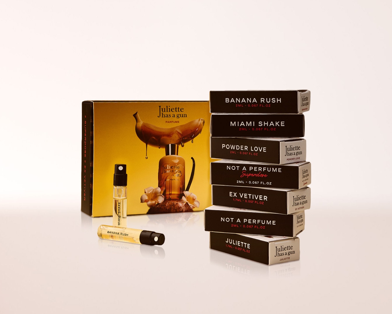 Das Juliette Has a Gun Parfümset enthält eine gelbe Box mit Bananenmotiv, eine große Parfümflasche, zwei kleine Probenflaschen und einen Stapel kleiner schwarzer Parfümprobenboxen.