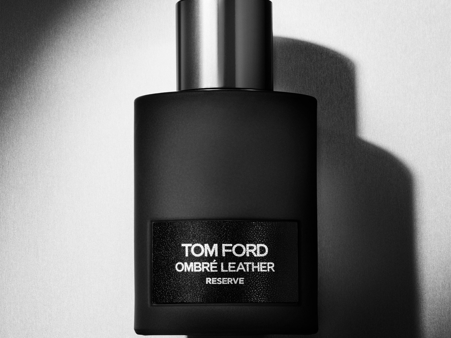Der Duft Tom Ford Ombré Leather Reserve präsentiert sich in einem eleganten, mattschwarzen Flakon mit einem silbernen Deckel und einem strukturierten Etikett, das den Namen des Parfums in Weiß hervorhebt.