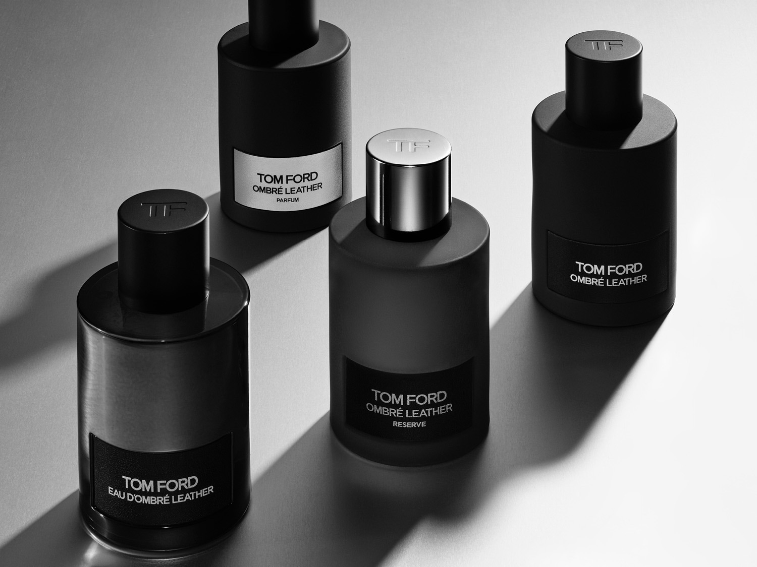 Vier schwarze, zylindrische Tom Ford Ombré Leather Parfümflaschen stehen auf einer hellgrauen Oberfläche.