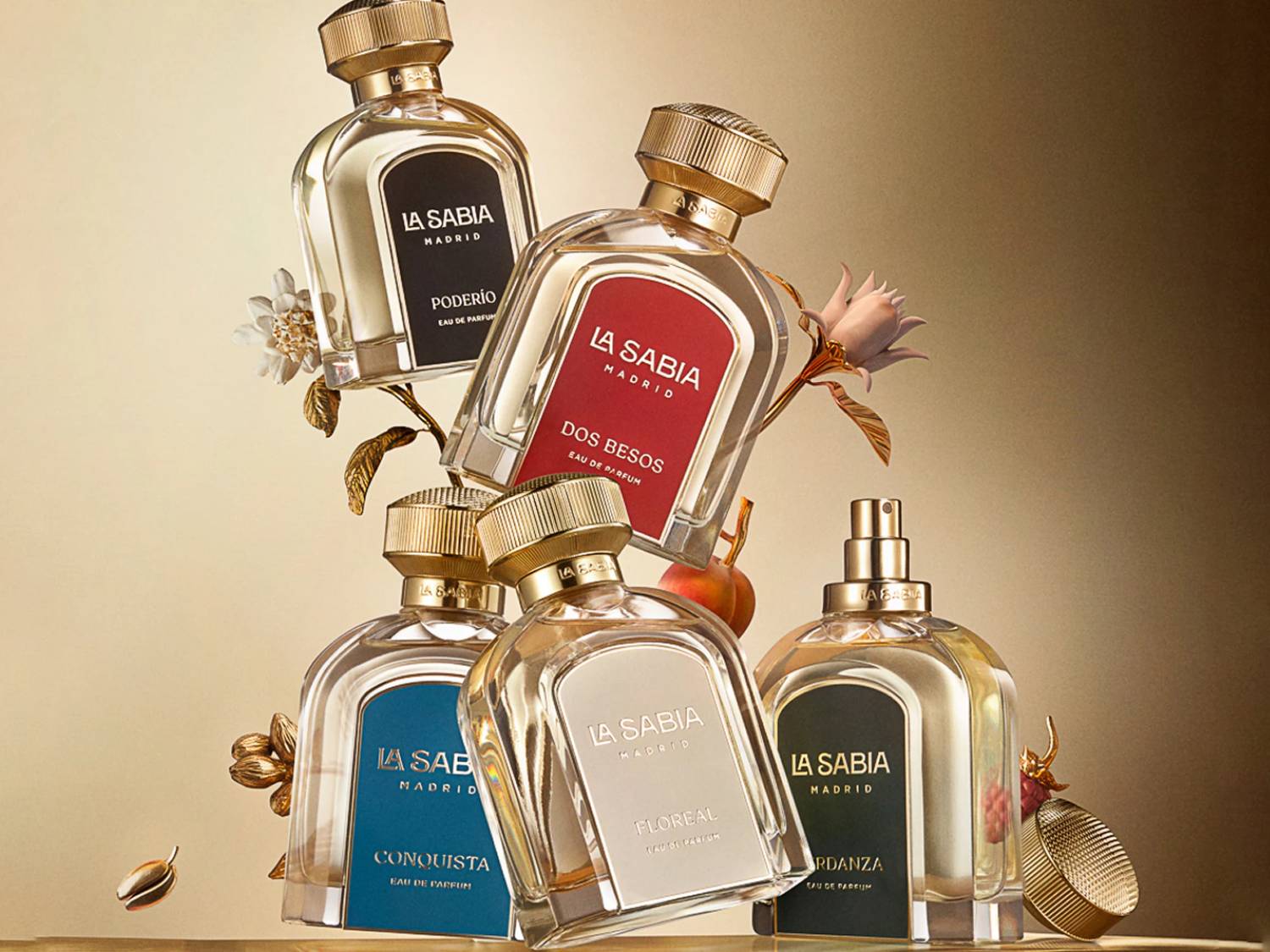 Pięć eleganckich flakonów perfum La Sabia Madrid, każdy z inną etykietą w kolorach czarnym, czerwonym, niebieskim, białym i zielonym, otoczonych złotymi liśćmi i kwiatami, prezentuje różnorodność zapachów.