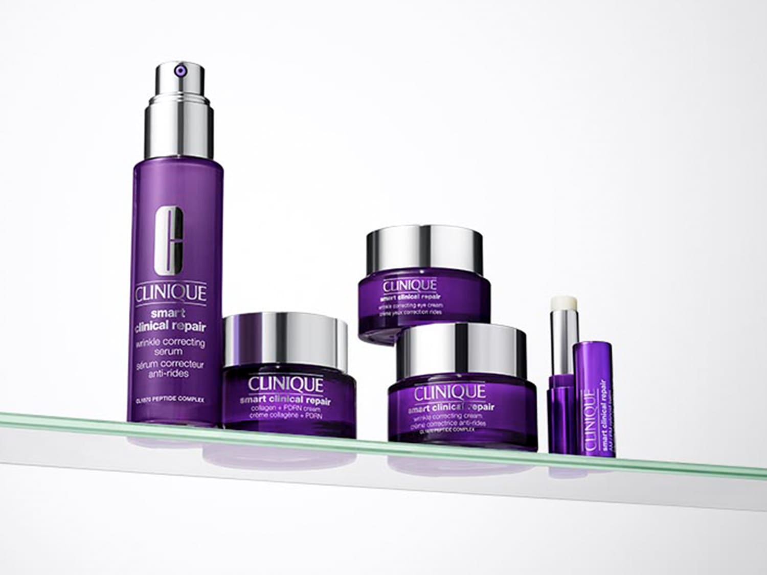 Una collezione di prodotti Clinique Smart Clinical Repair, tra cui un siero viola con erogatore argentato, creme in vasetti viola con coperchi argentati e un balsamo labbra viola, tutti esposti su una mensola di vetro.