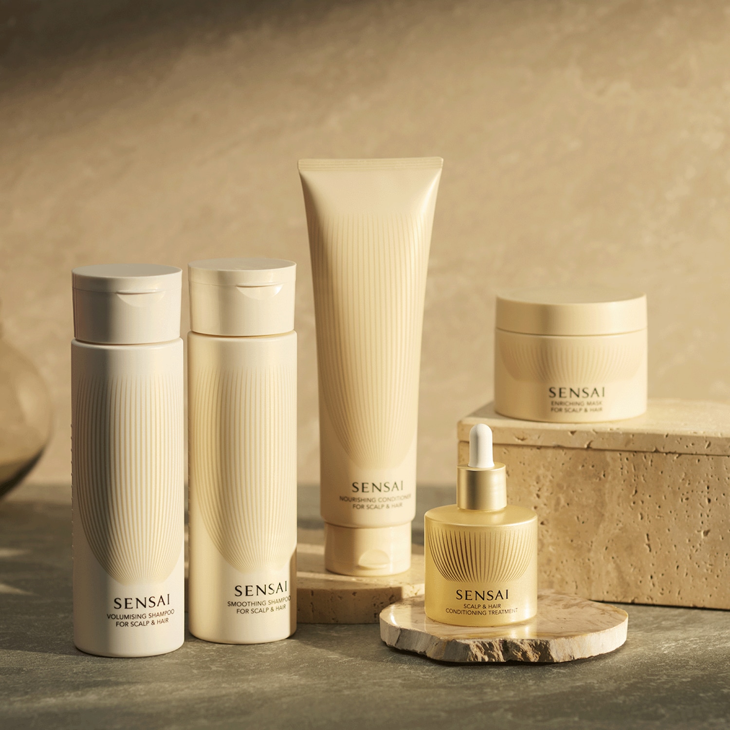 Découvrez la gamme complète de soins capillaires Sensai, comprenant un shampoing volumisant, un shampoing lissant, un après-shampoing nourrissant, un masque enrichissant et un traitement revitalisant pour le cuir chevelu et les cheveux, tous présentés dans des emballages élégants de couleur crème.
