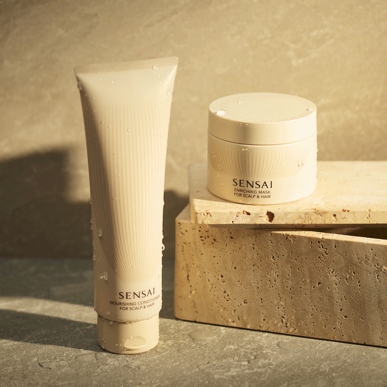 Le revitalisant nourrissant et le masque enrichissant Sensai pour le cuir chevelu et les cheveux sont présentés dans des emballages crème élégants, parfaits pour une routine de soins capillaires luxueuse.