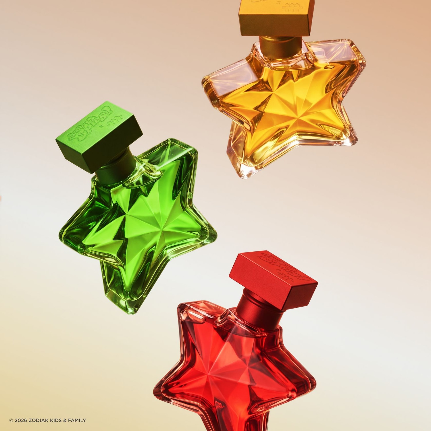 Trois flacons de parfum en forme d'étoile, un vert, un rouge et un doré, flottent dans les airs, chacun avec un bouchon de couleur assortie.