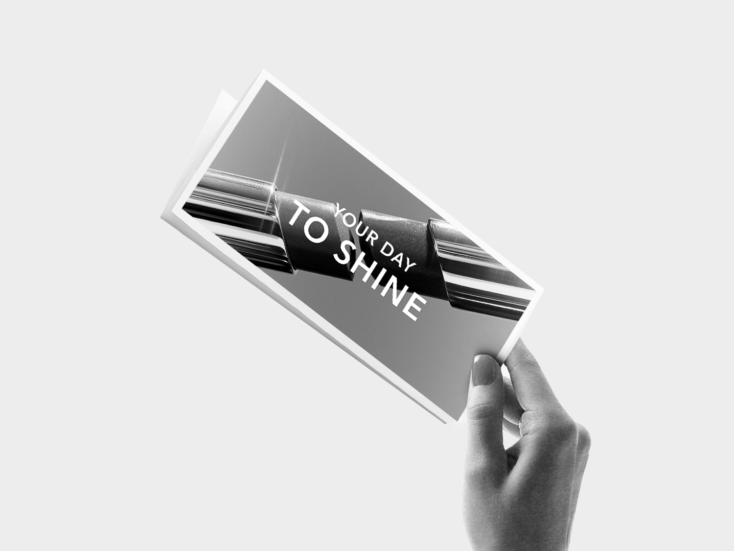 Ruka drží černobílou kartu s textem „YOUR DAY TO SHINE“.
