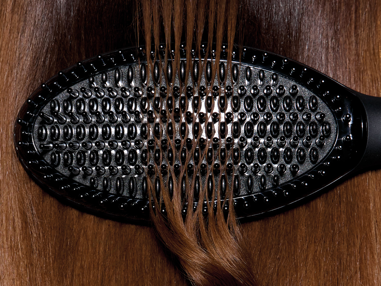 Eine schwarze Haarbürste mit vielen kleinen Noppen gleitet durch glänzendes, braunes Haar und entwirrt es sanft.