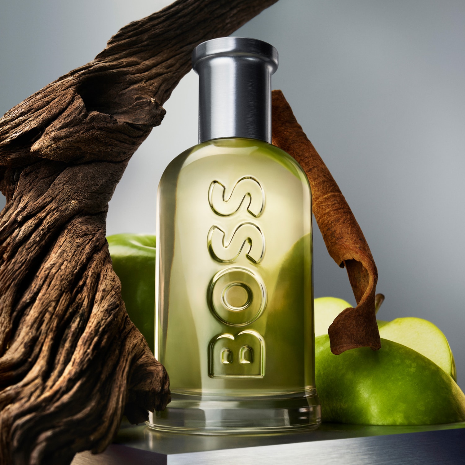 Parfum BOSS s jablkom, škoricou a drevom v pozadí, ktoré zvýrazňujú jeho prírodné zložky.