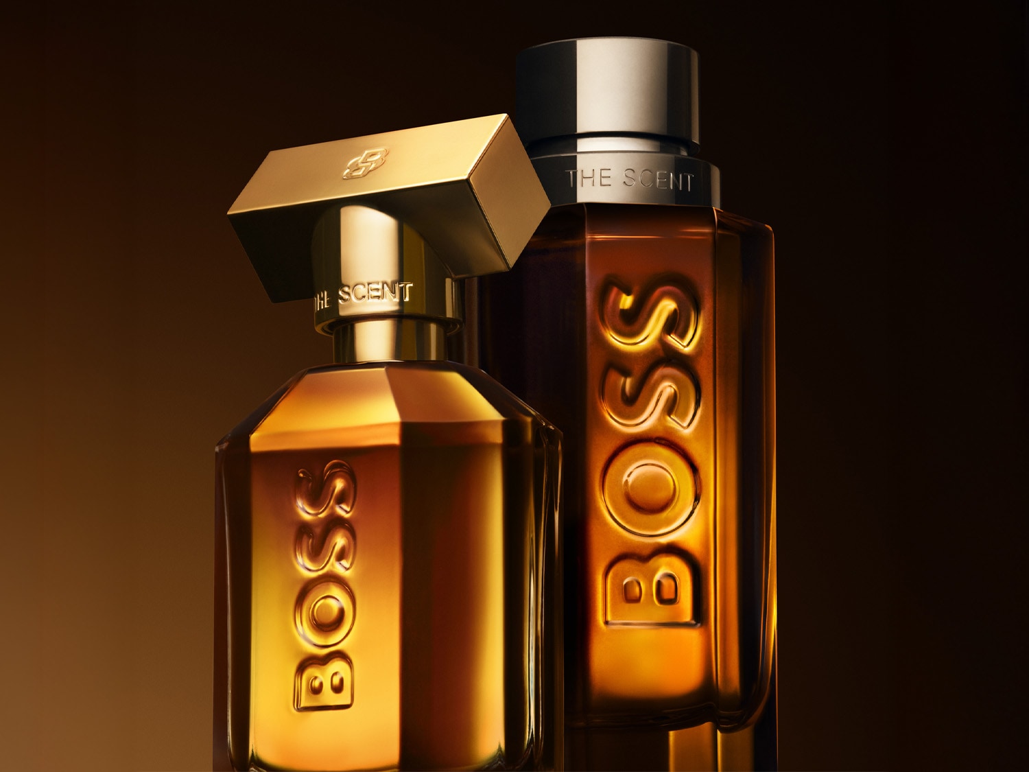 Dve fľaštičky parfumu Boss The Scent v tvare flakónu v odtieňoch jantárovej a zlatej farby, s nápisom „BOSS“ vyrazeným na prednej strane a „THE SCENT“ na uzávere.