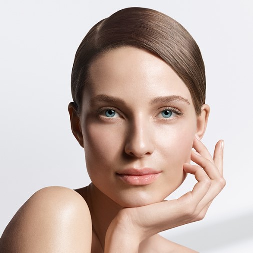 Portret kobiety o jasnej cerze, z gładko zaczesanymi brązowymi włosami i niebieskimi oczami, delikatnie dotykającej dłonią policzka.