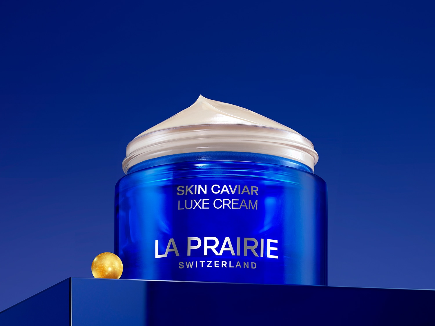 Modrý kelímek La Prairie Skin Caviar Luxe Cream s bílým krémem na vrchu a zlatou kuličkou, která symbolizuje luxus a švýcarskou kvalitu.