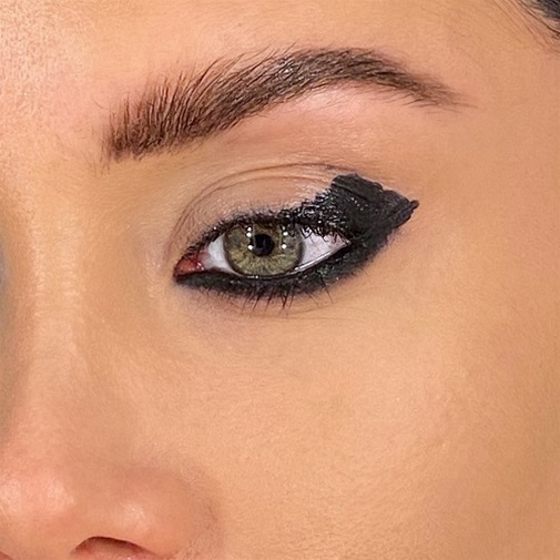 Primo piano di un occhio verde truccato con eyeliner nero spesso e drammatico, che mette in risalto la forma e l'intensità dello sguardo.