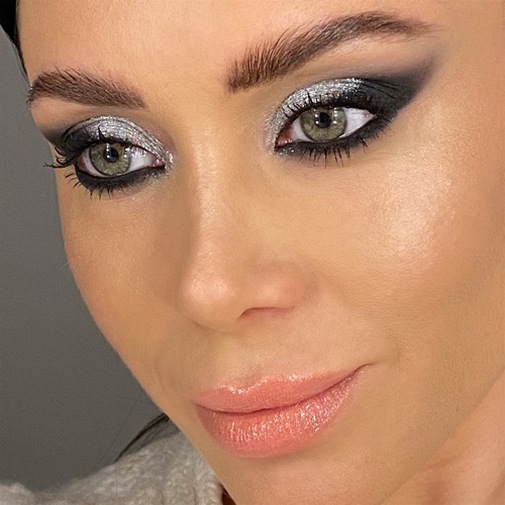 Primo piano di un volto femminile con occhi truccati con ombretto argento glitterato e nero sfumato, labbra lucide color pesca.