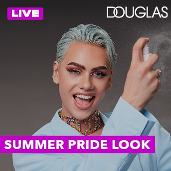 Een vrolijke persoon met blauw haar en een kleurrijke ketting, spuitend met een flesje, met de tekst 'LIVE' en 'SUMMER PRIDE LOOK'.