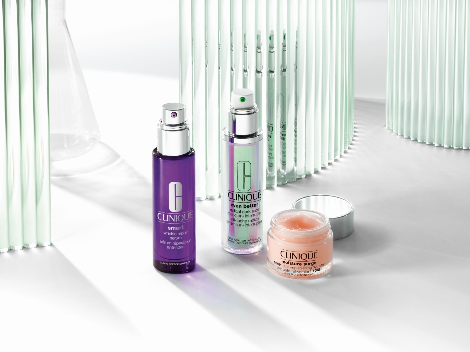 Fioletowe serum Clinique Smart Wrinkle Repair, serum Clinique Even Better w opalizującej butelce i krem nawilżający Clinique Moisture Surge w słoiczku.